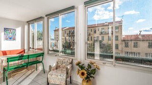 A bright room with large windows, a green bench, a floral chair, and a vase with sunflowers. - Appartement California - Welkeys (Nice)