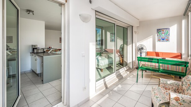 A modern living room with a sofa, a table, and a green chair. There is a sliding glass door leading to a kitchen and a dining area. - Appartement California - Welkeys (Nice)