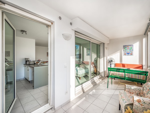 Una sala moderna con un sofá, una mesa y una silla verde. Hay un ventanal corredero que da a una cocina y un comedor.