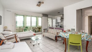 A modern living room with a sofa, a glass coffee table, and a dining area with a table set for two. - Appartement California - Welkeys (Nice)