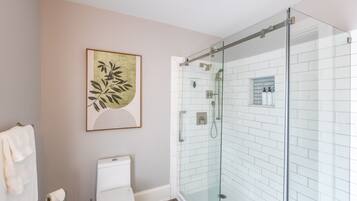 Un baño con ducha separada por vidrio, inodoro y una obra de arte enmarcada en la pared.