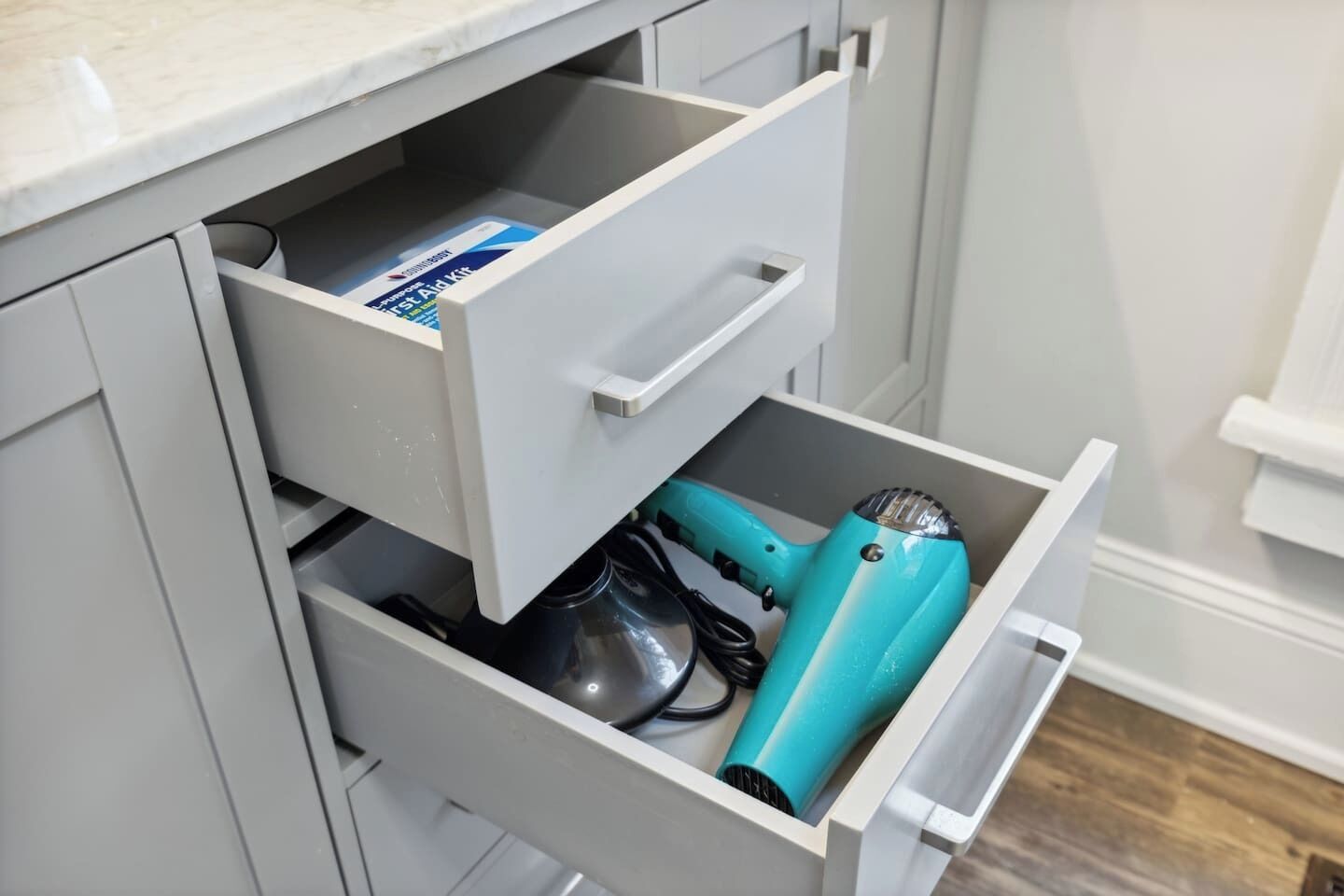 Un cajón de cocina con un secador azul, un recipiente negro y una caja de botiquín de primeros auxilios.