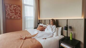 A hotel room with a bed, a bedside table with a lamp, a water bottle, and a wall art piece.