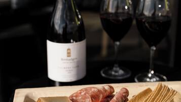Una taula de tall de fusta amb una llesca de formatge, làmines de salami i galetes. Al fons, hi ha una ampolla de vi i dues copes de vi vermell.