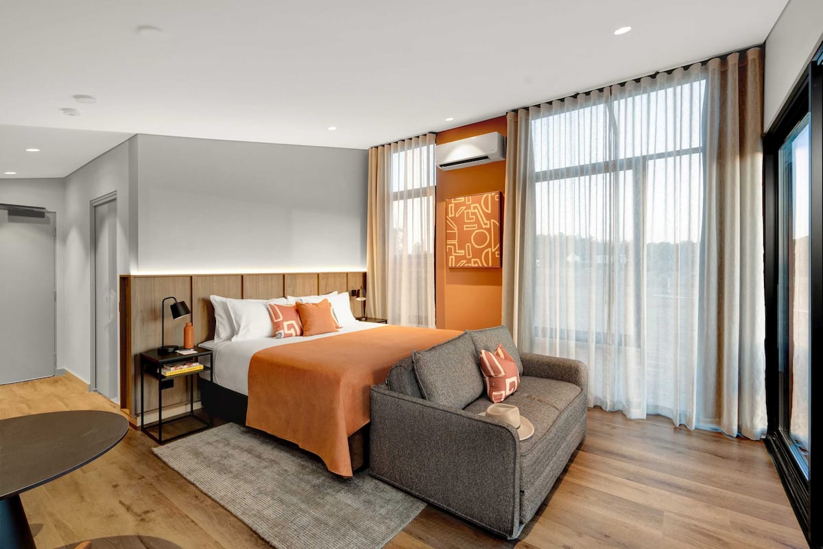 Una habitación de hotel moderna con una cama grande, un sofá, un escritorio y vistas a la ciudad.