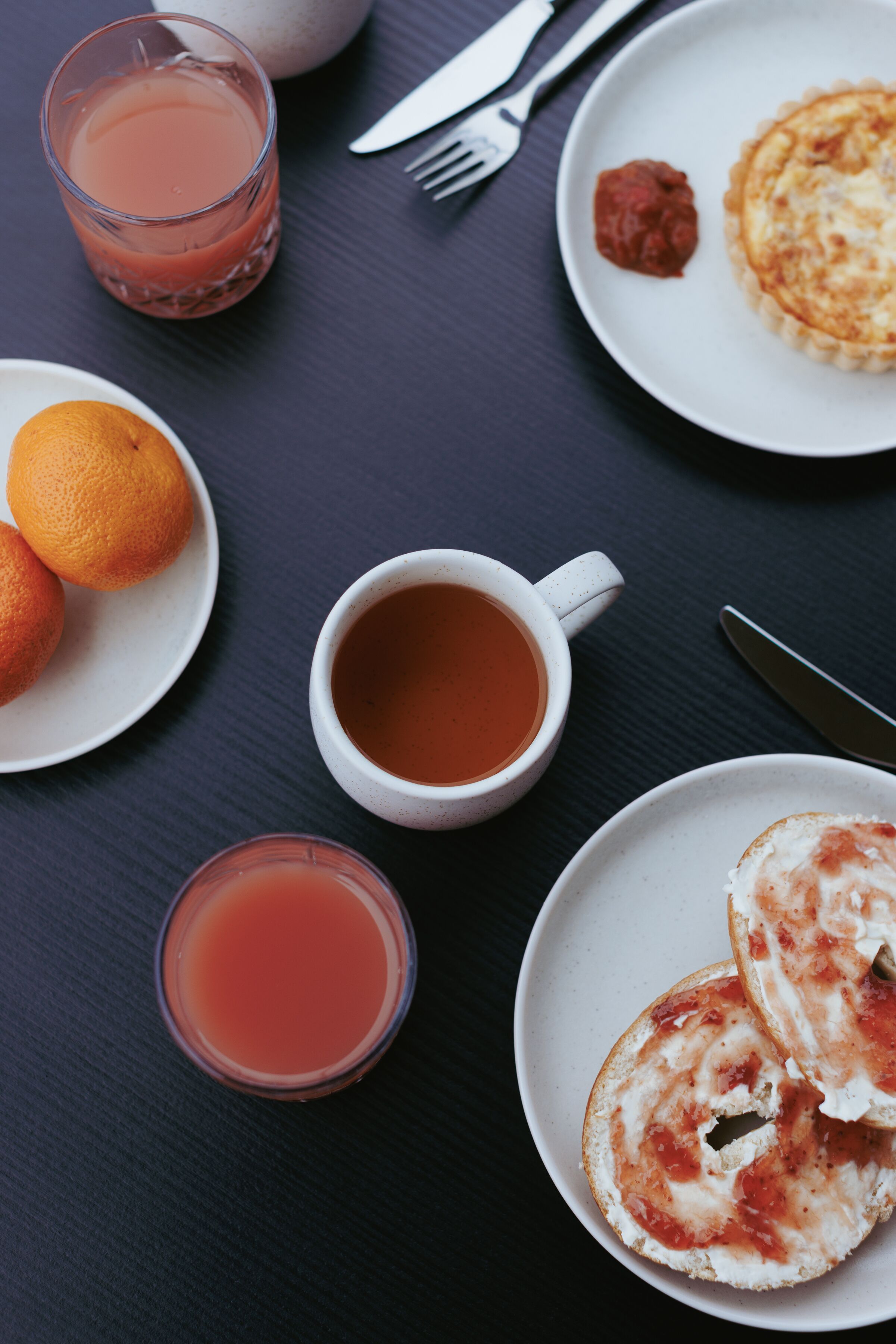 Una mesa con una porción de panqueques, un vaso de jugo, una taza de té y un plato de naranjas.