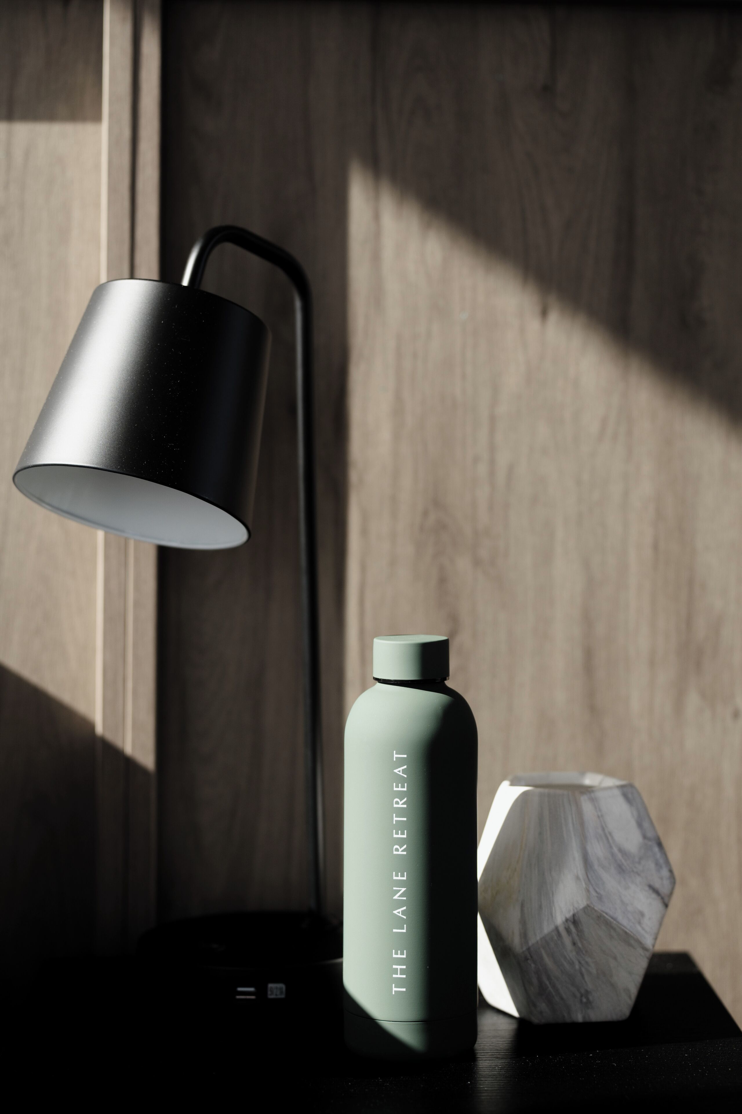 A modern lamp, a water bottle, and a hexagonal object on a wooden surface.