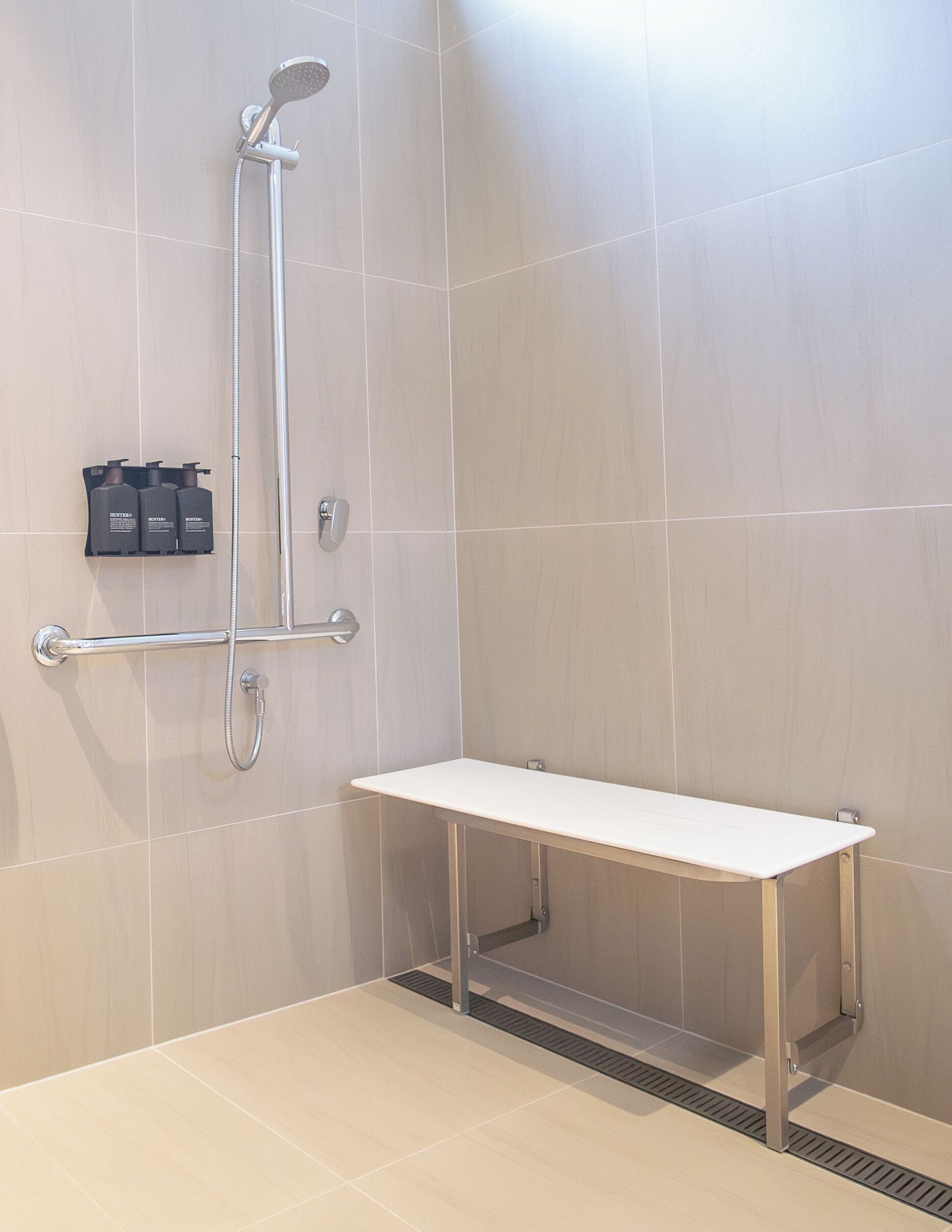Een moderne douche met een handdouche, een extra douchestraal en een bankje.