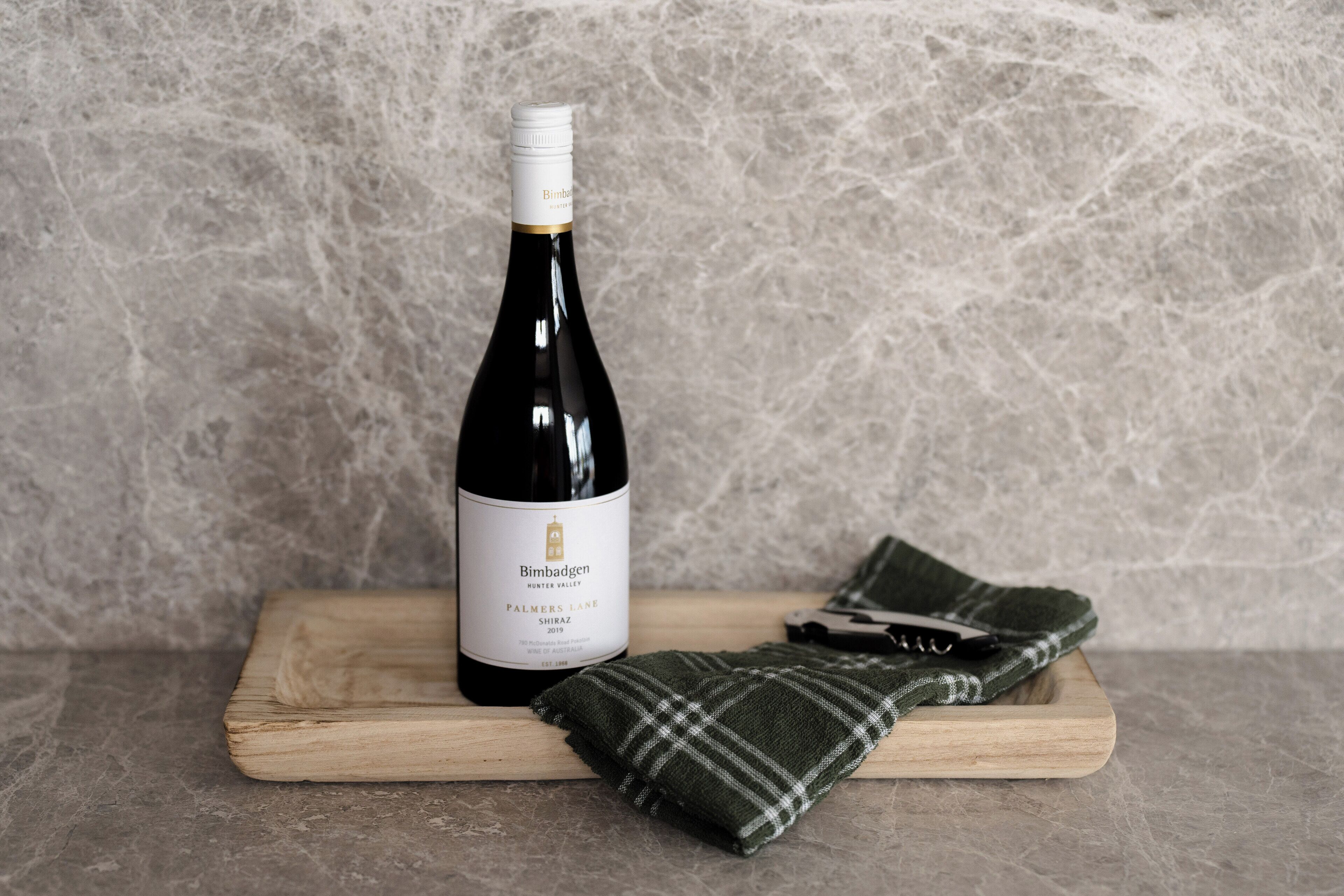 A bottle of wine on a wooden board with a plaid cloth beside it.