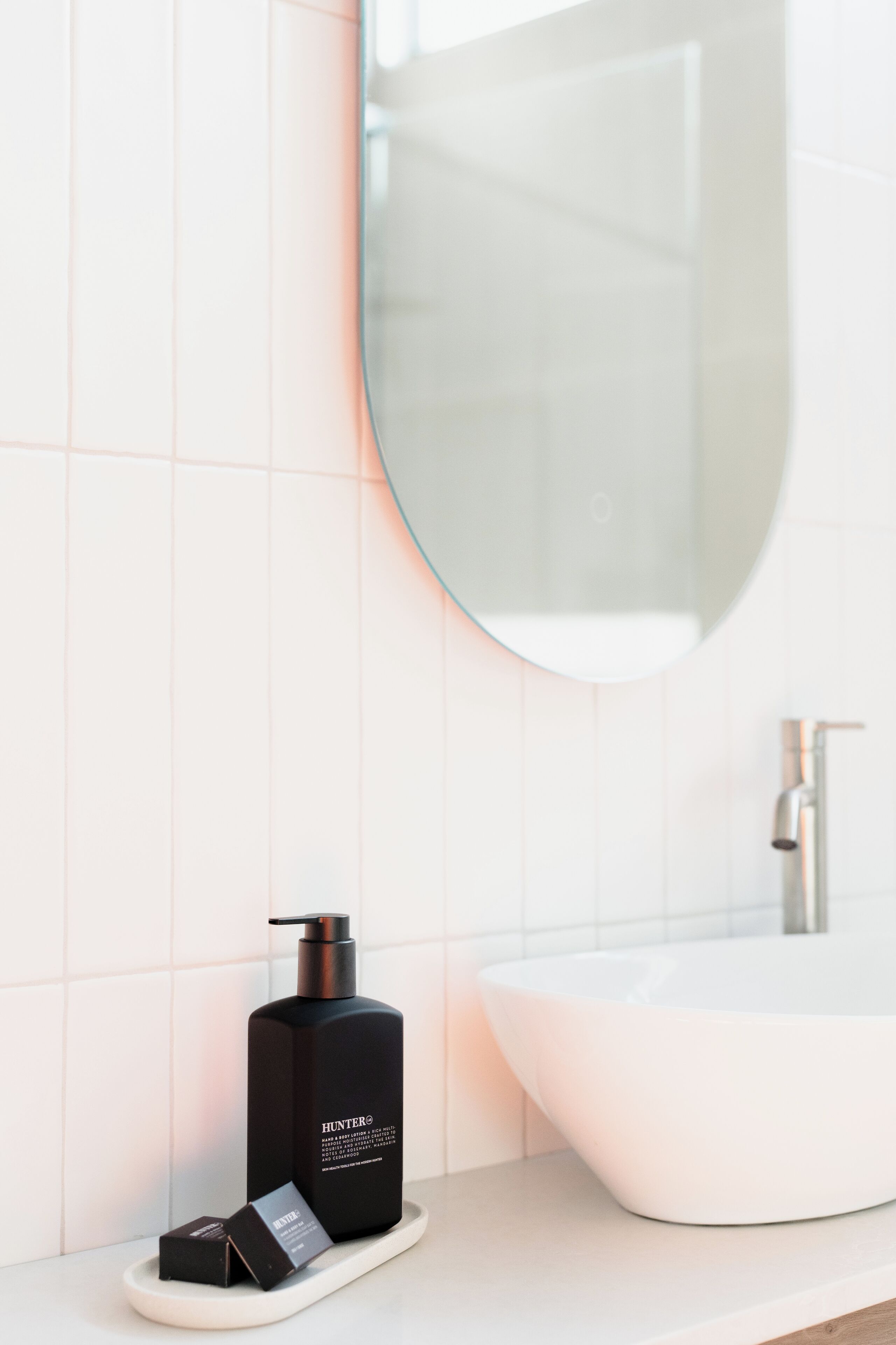 A bathroom with a white sink, a black bottle, and a mirror.
