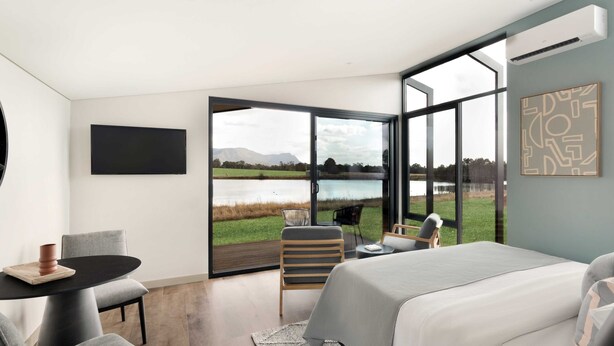 Un dormitorio moderno con una cama grande, un escritorio y una silla. Cuenta con un ventanal con vistas a un lago y montañas.