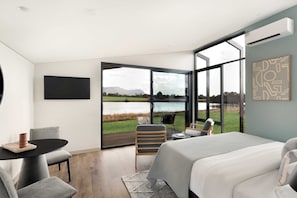 Un dormitorio moderno con una cama grande, un escritorio y una silla. Cuenta con un ventanal con vistas a un lago y montañas.