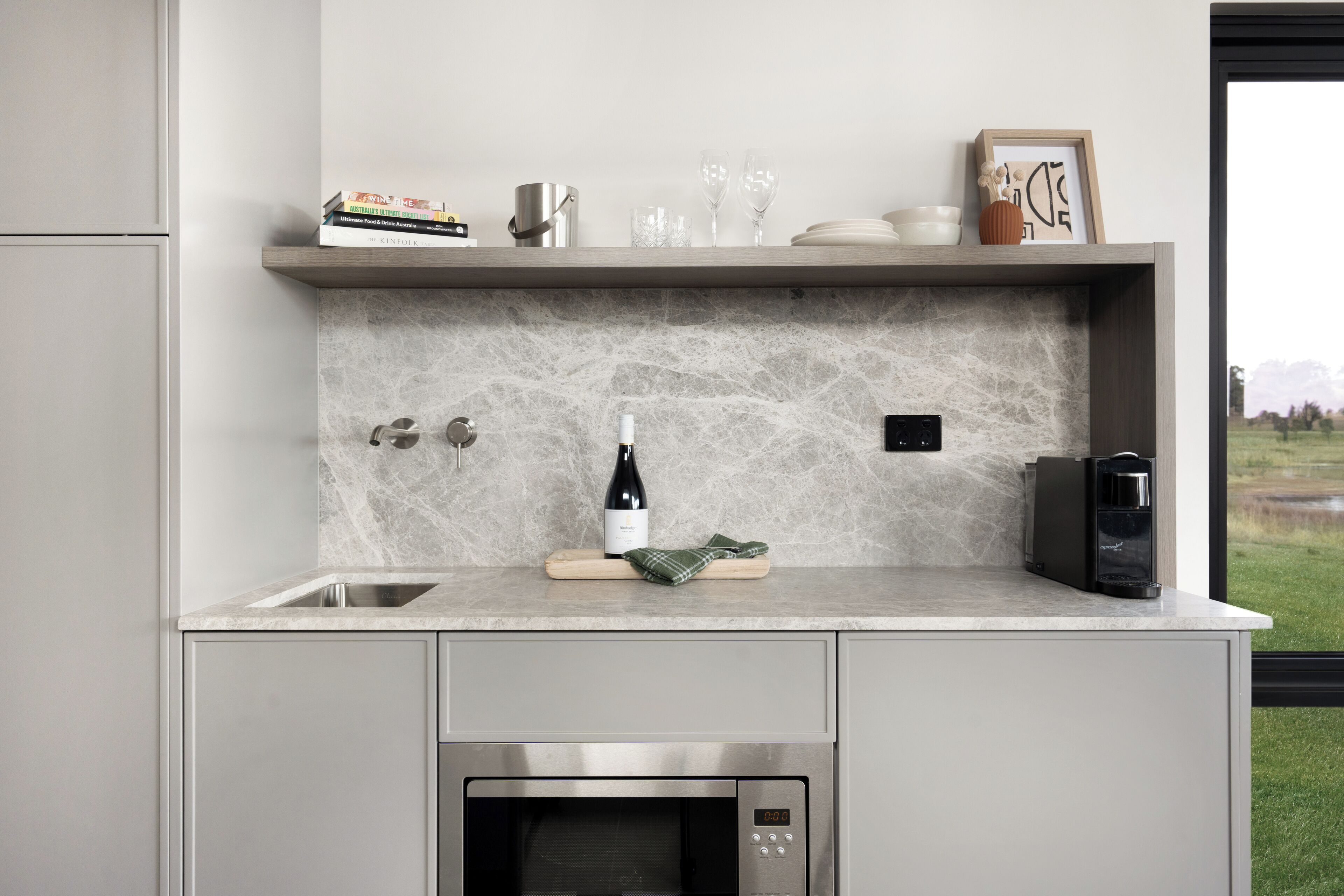 Una cocina moderna con horno empotrado, una botella de vino y una cafetera sobre la encimera.
