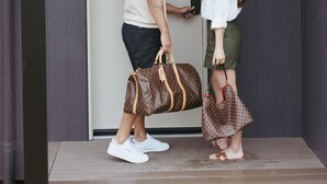 Un hombre y una mujer están de pie frente a una puerta con el número 41, sosteniendo bolsos de mano.