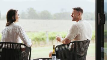 Two people sitting at a table with a bottle of wine and glasses, outdoors with a view of a field.