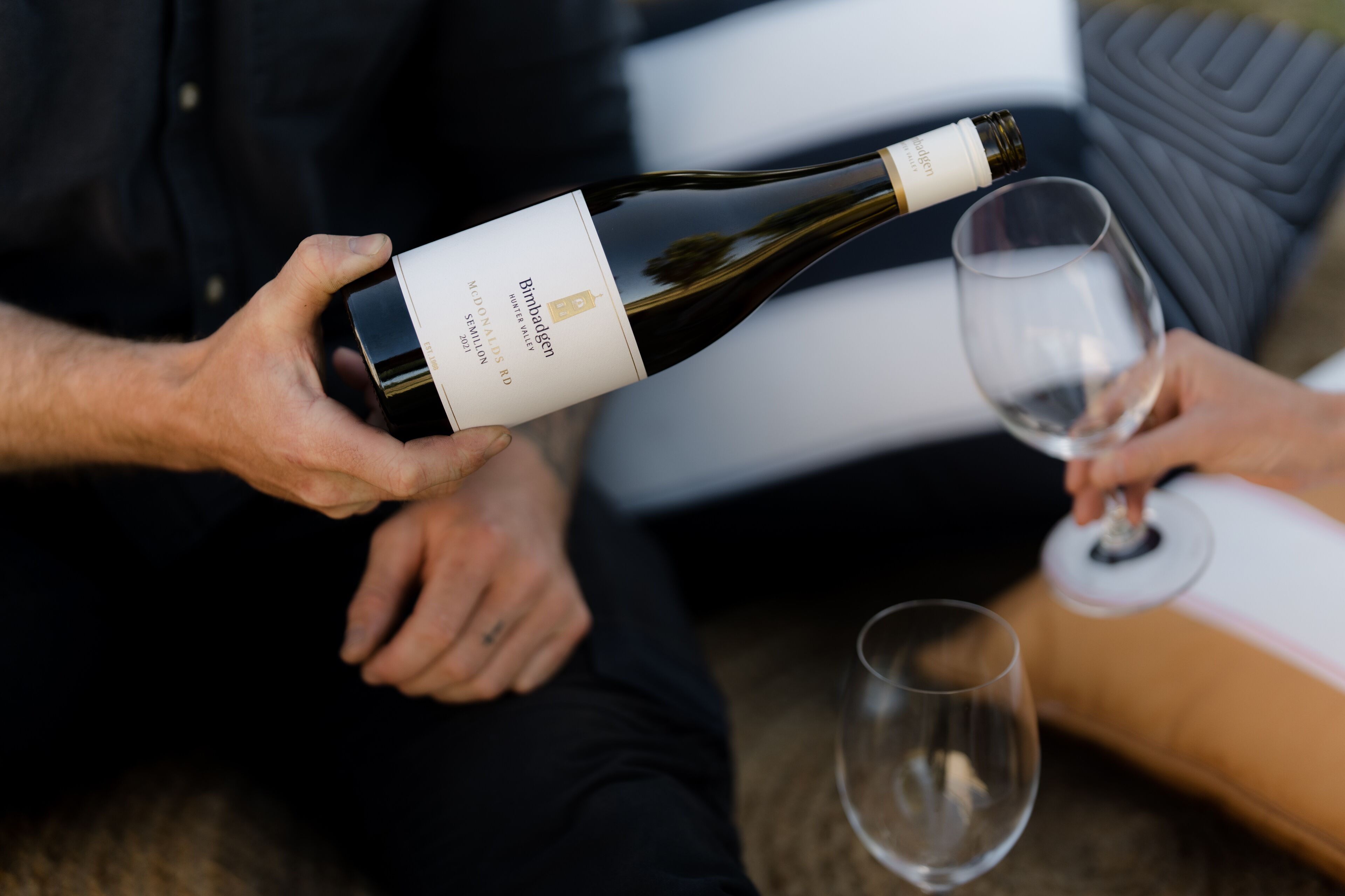 Una persona sosteniendo una botella de vino y sirviéndolo en una copa.