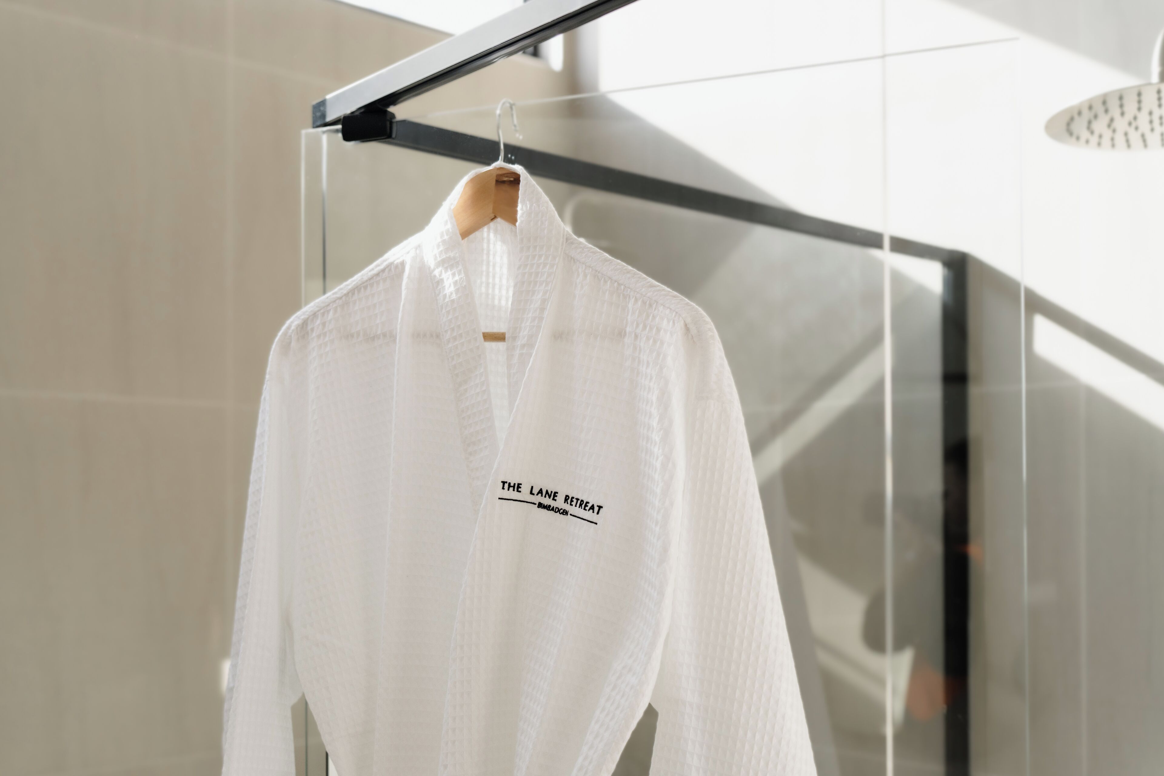 A white robe hanging on a rack in a modern, well-lit room with a glass partition and a metal railing.