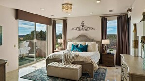 Une chambre avec un grand lit, une porte vitrée donnant sur un balcon, un lustre et une commode.