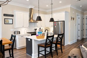 A modern kitchen with white cabinetry, a stainless steel refrigerator, and a central island with chairs.