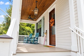 A porch with a wooden ceiling, a lantern, and a door with a flower arrangement.