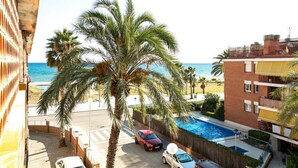 A balcony with a view of the sea, a swimming pool, and a red car parked in front.