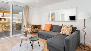 A modern living room with a grey sofa, a small round table, a chair, a large mirror, and a floor lamp.