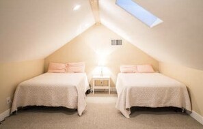 A small, cozy attic bedroom with two beds, a nightstand, and a skylight.
