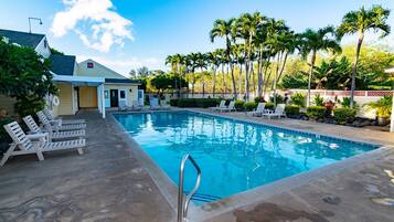 A swimming pool with lounge chairs, palm trees, and a building with a garage.