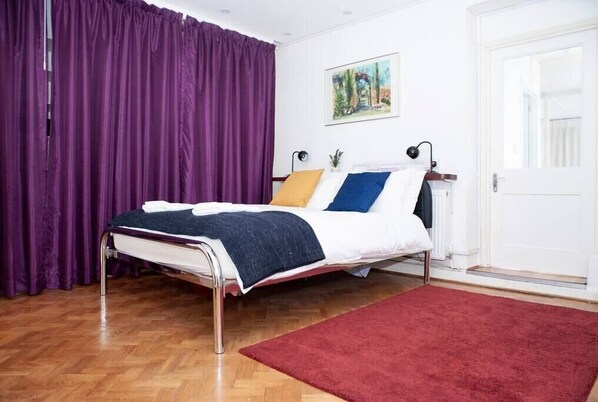 Una cama bien hecha con una alfombra roja, una cortina morada y un cuadro en la pared.