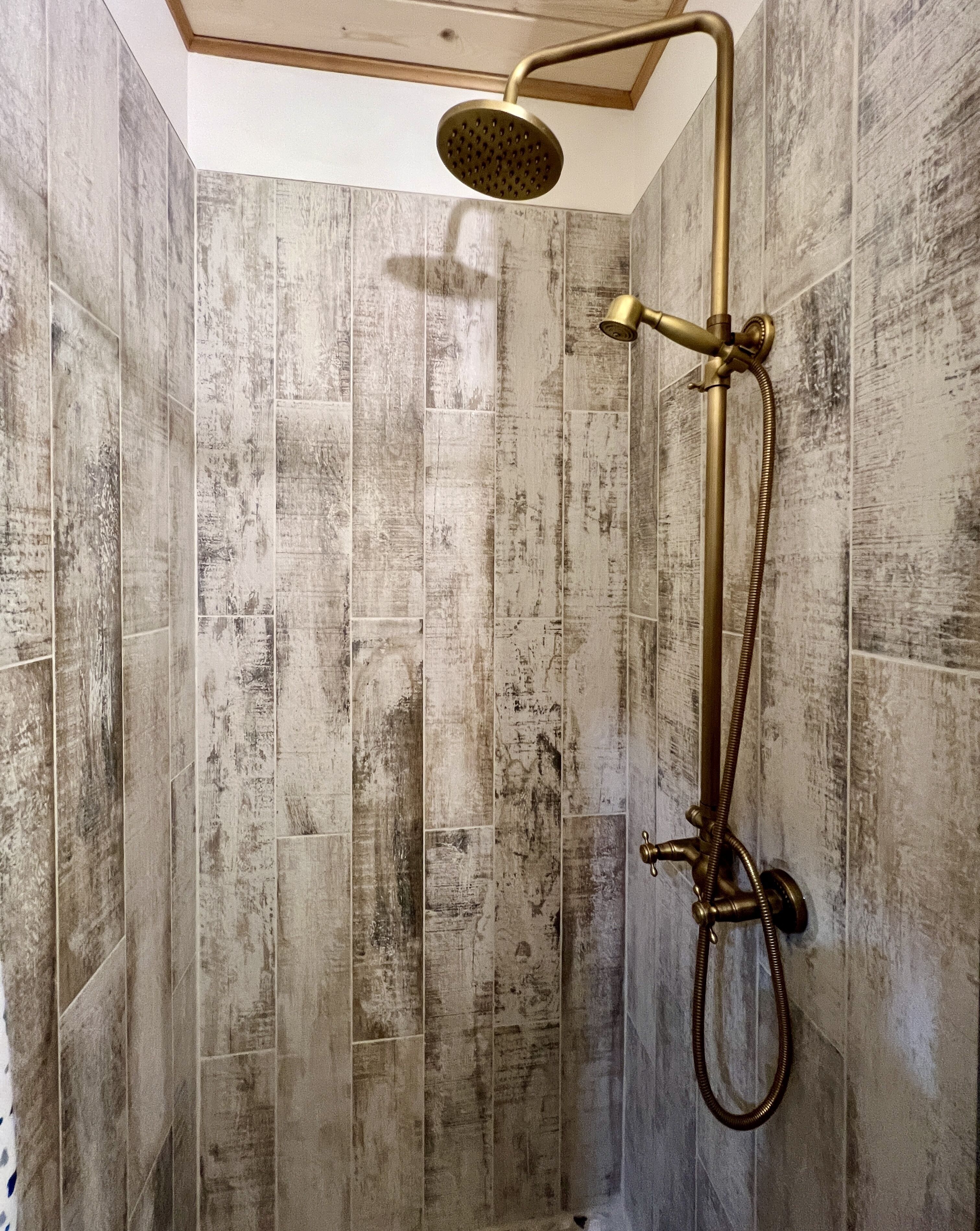 Een douche met een ronde douchekop en messing beslag in een kamer met verticale, houtstructuur muren.