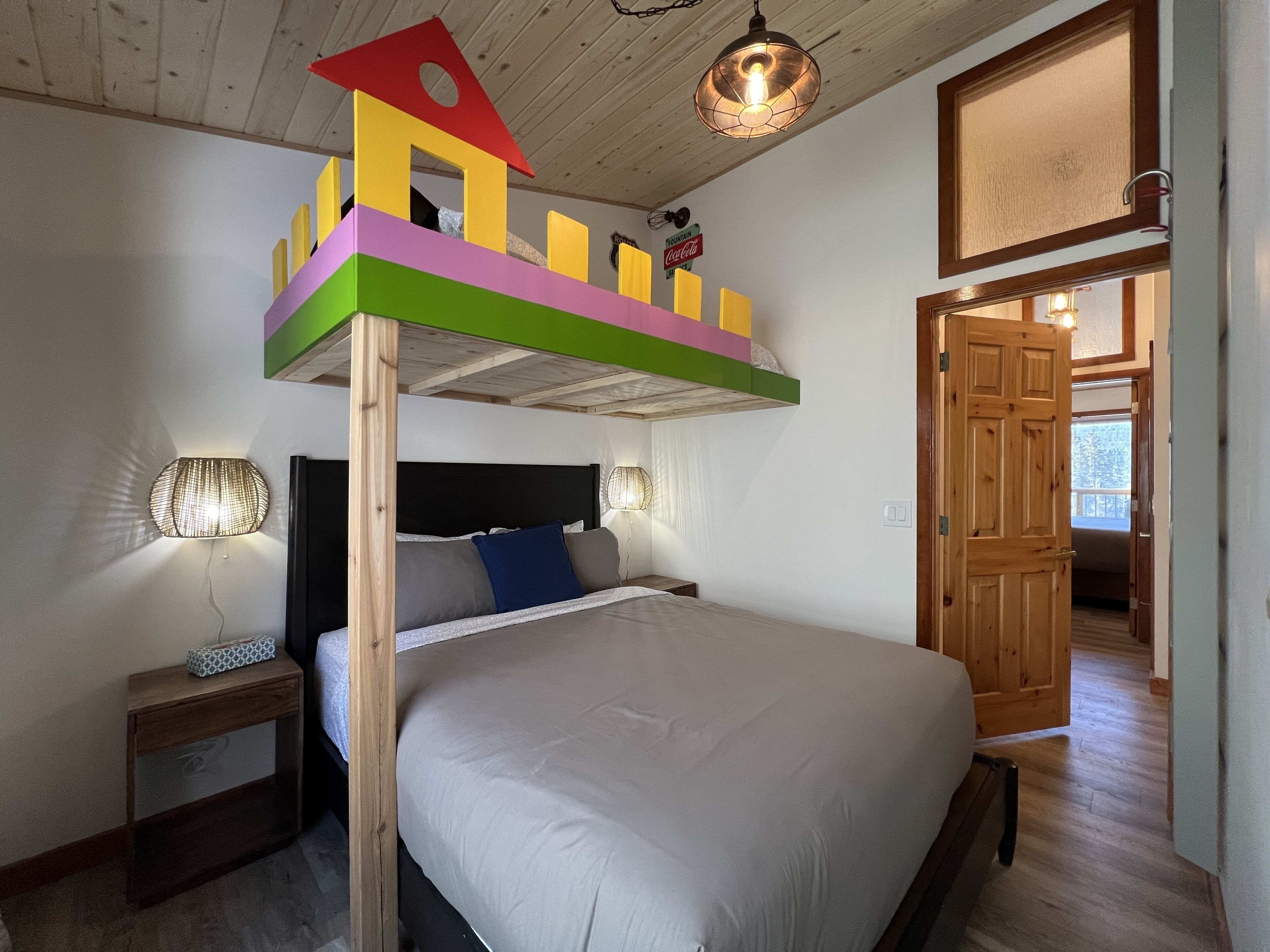 Quarto com cama de solteiro, mesa de cabeceira com abajur e porta de madeira que dá para outro cômodo.