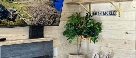 Uma sala de estar moderna com televisão de tela plana, estantes de madeira com plantas e um letreiro escrito 'Relax'.