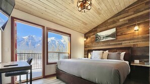 Un dormitorio con cama, escritorio y silla, una ventana grande con vista a la montaña y paredes de madera.