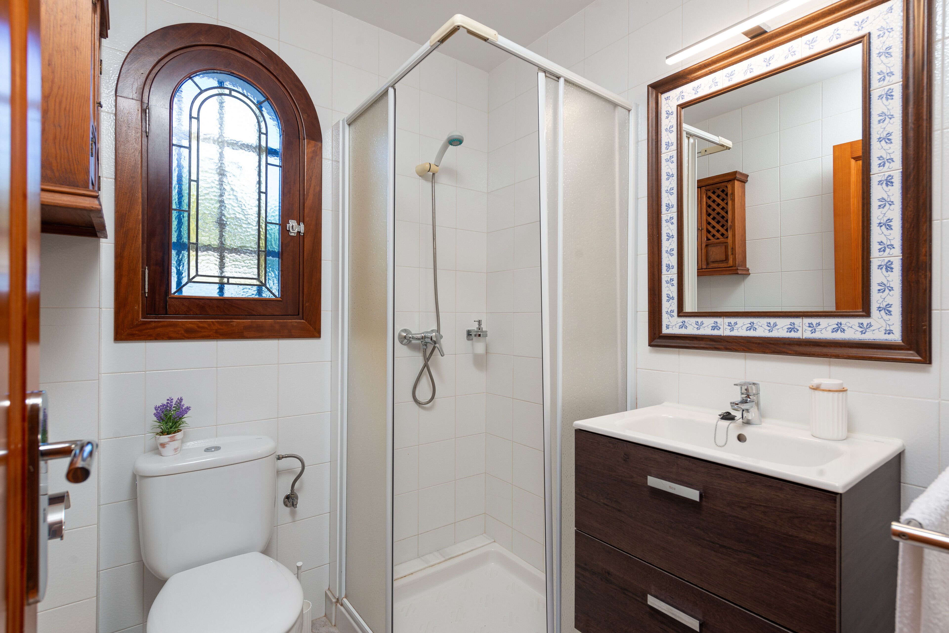 Een badkamer met toilet, douche, wastafel en spiegel met decoratieve lijst.