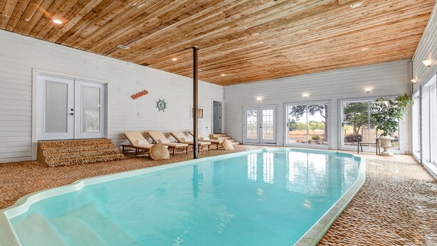 Piscina con escalones de acceso, rodeada de sillones de descanso y un techo de madera.