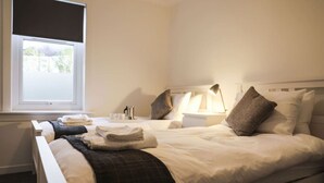 A hotel room with two beds, a window, a bedside table with a lamp, and a view of the outdoors.