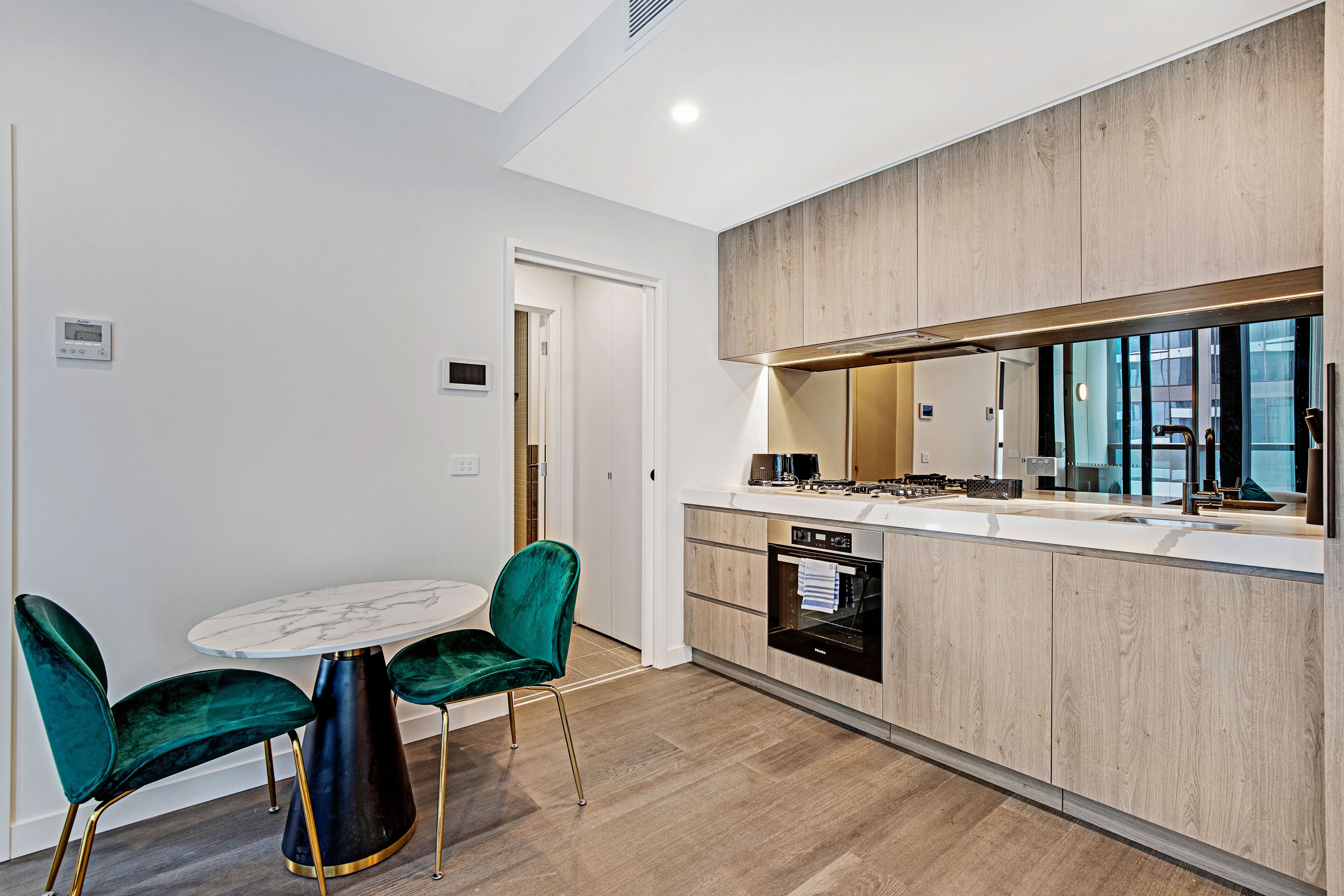 Una cocina moderna con una mesa de mármol, sillas verdes y armarios de madera.