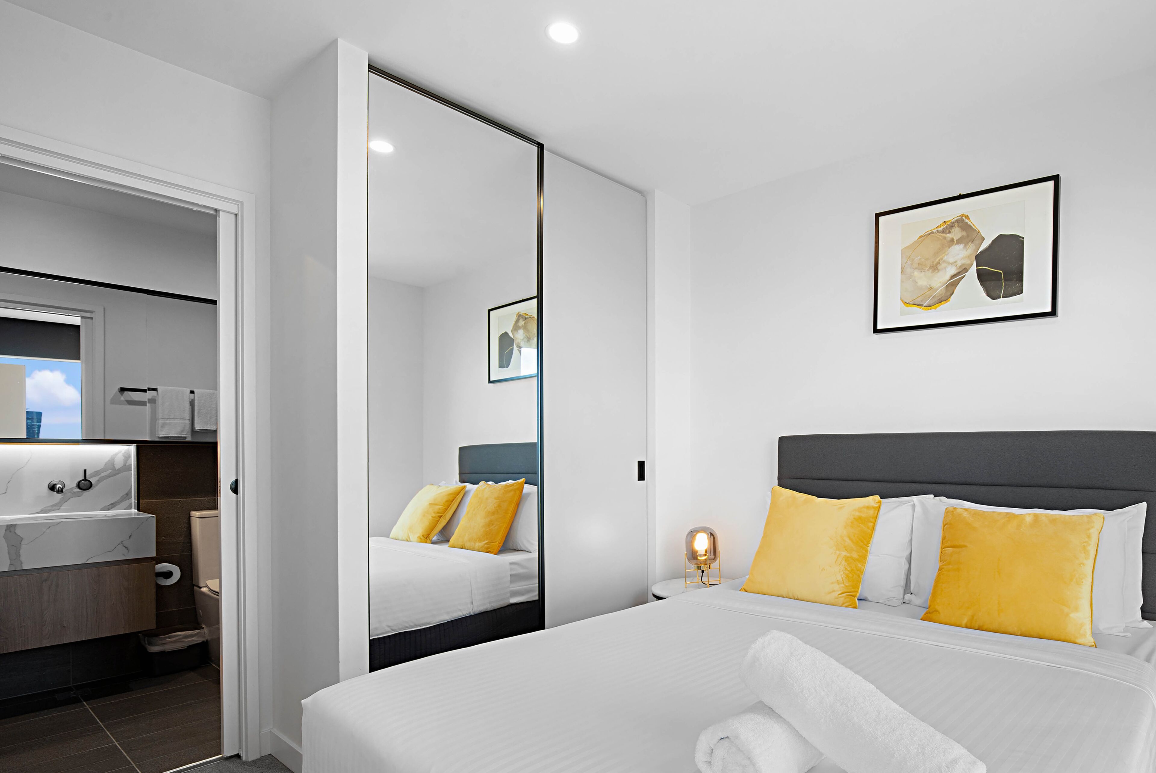 Una habitación de hotel moderna con una cama grande, una mesita de noche, un espejo y una obra de arte enmarcada en la pared.