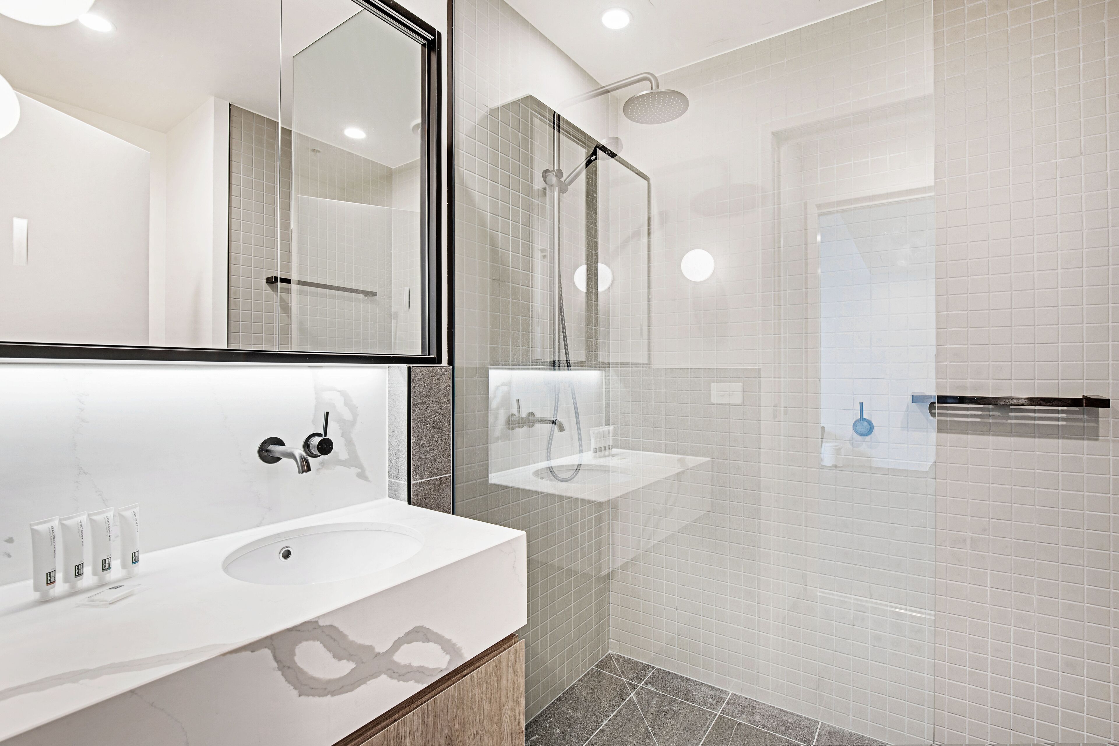 A modern bathroom with a large mirror, two sinks, a shower area, and a glass-enclosed shower.