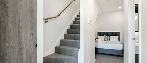 A staircase leading to a bedroom with a bed, a nightstand, and a headboard.