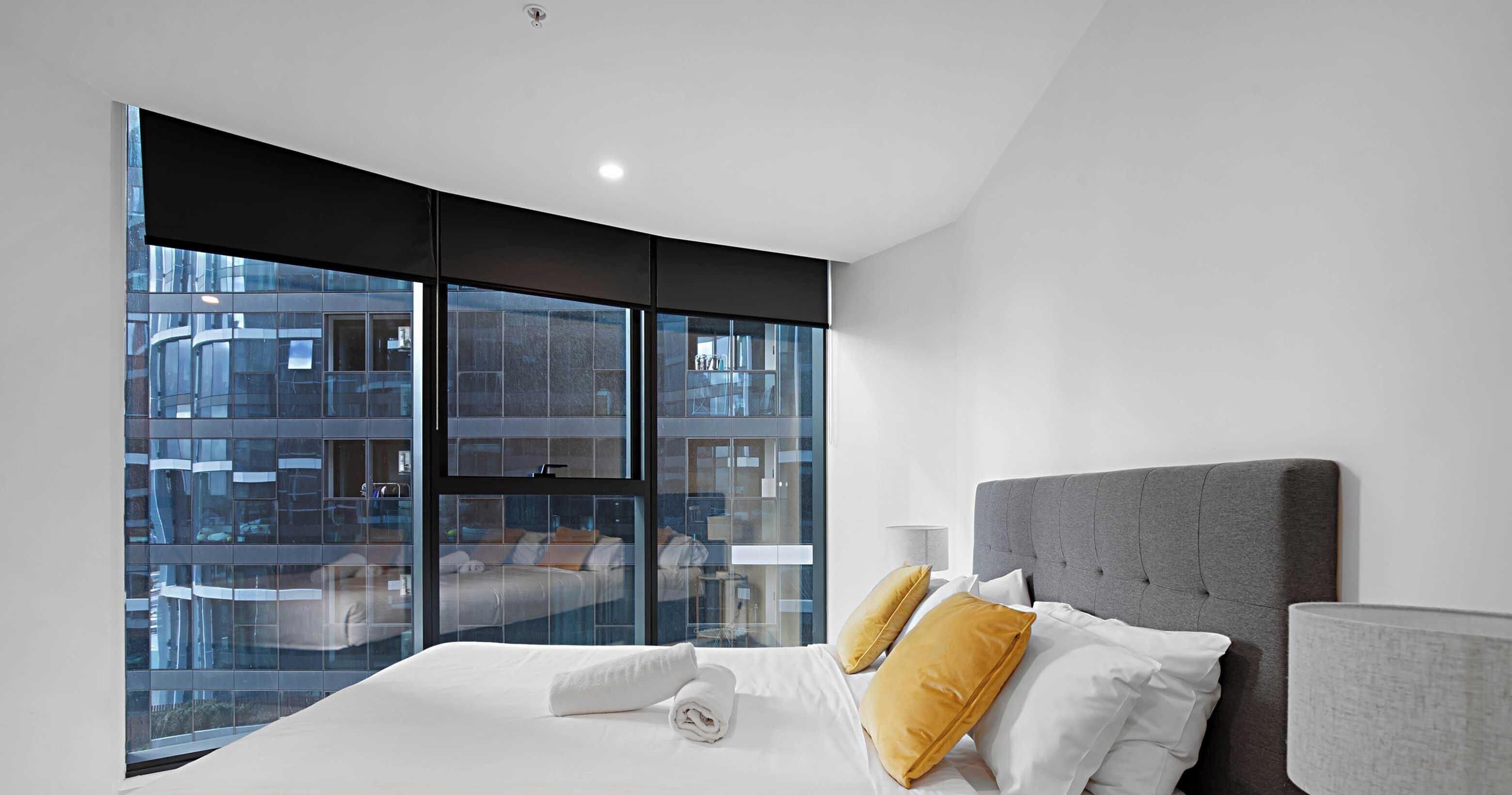 A modern hotel room with a curved window, a large bed with white linens, and a grey upholstered headboard.