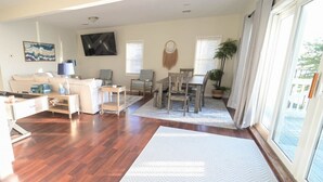 A spacious living room with a wooden floor, a sofa, a coffee table, and a TV mounted on the wall. - Penthouse | Historic Oneida Lakefront Condo 5 (Blossvale)