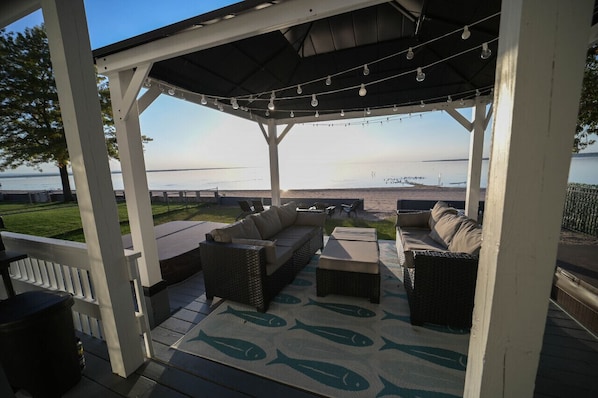 A covered outdoor seating area with a view of the water, featuring wicker furniture and string lights.