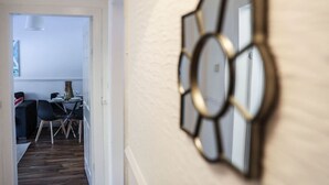 Een gang met een eethoek in de achtergrond, een decoratieve spiegel aan de muur en een deur.