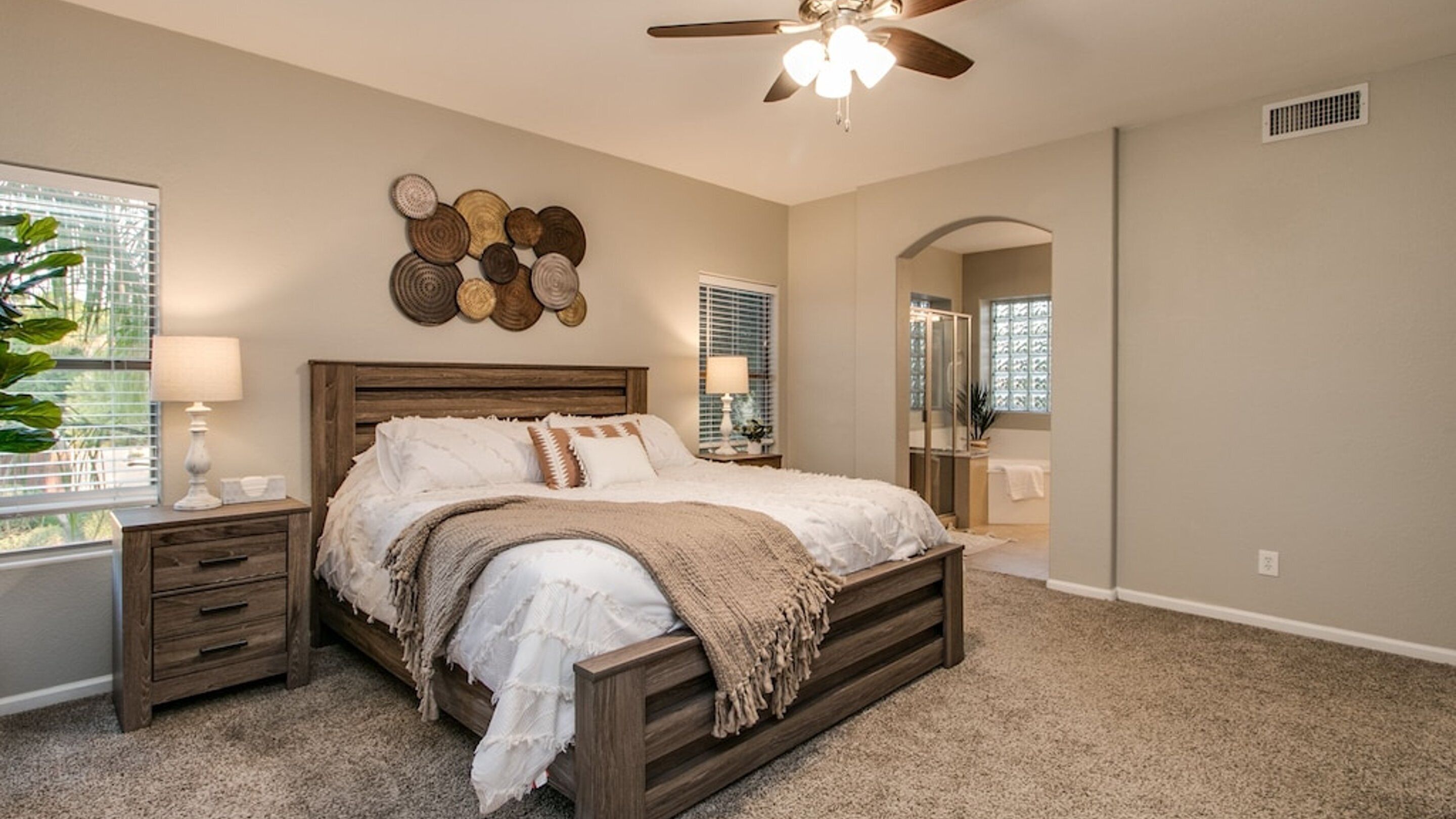A bedroom with a wooden bed, a ceiling fan, a wall art piece, and a window with blinds.