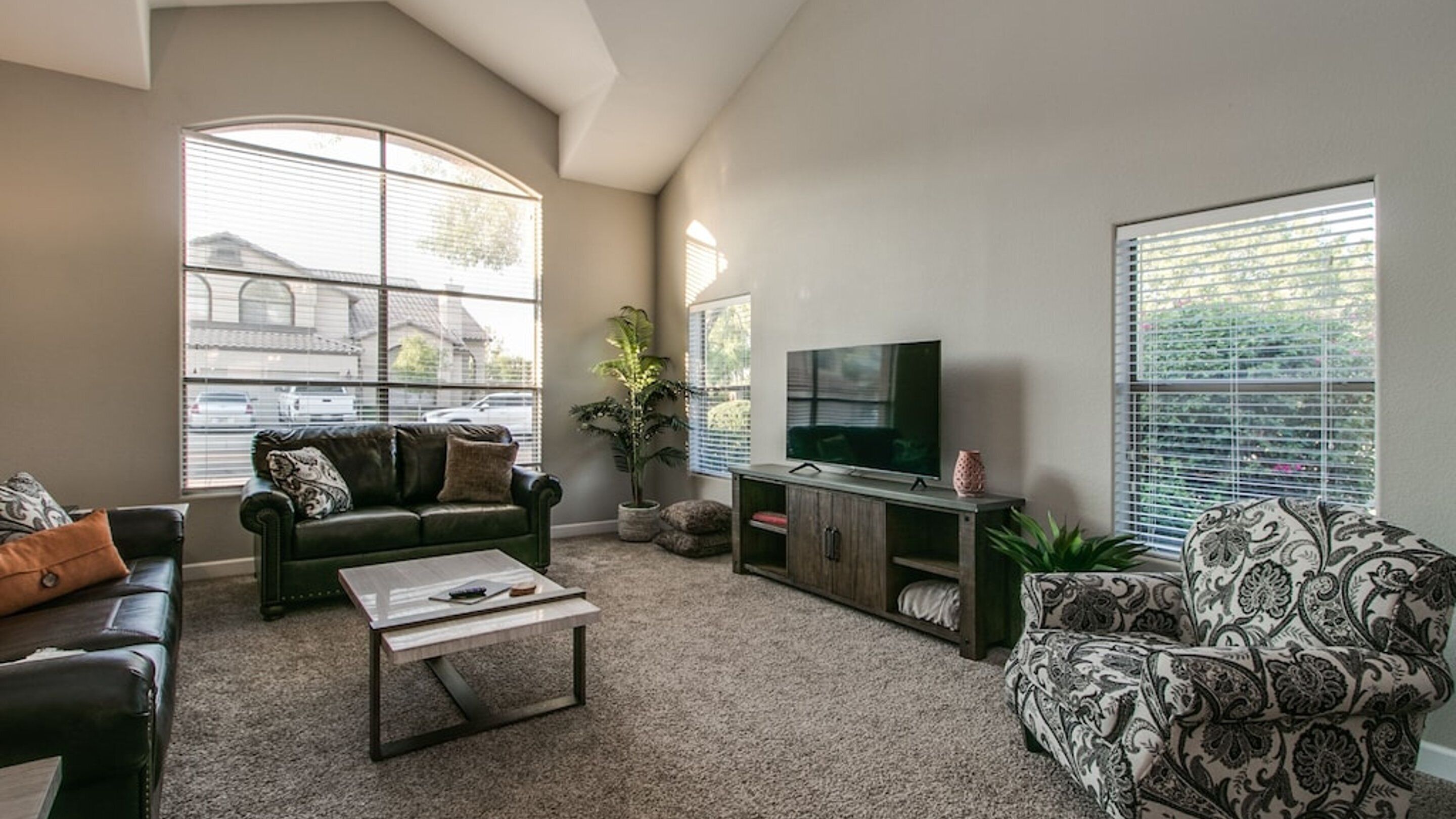 A living room with a sofa, a coffee table, a TV, and a patterned armchair.