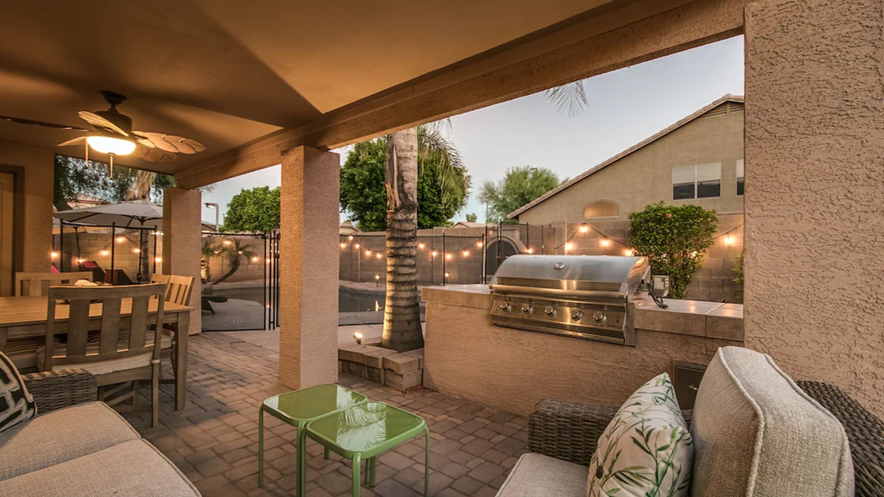 An outdoor patio with a dining table, chairs, a grill, and string lights.