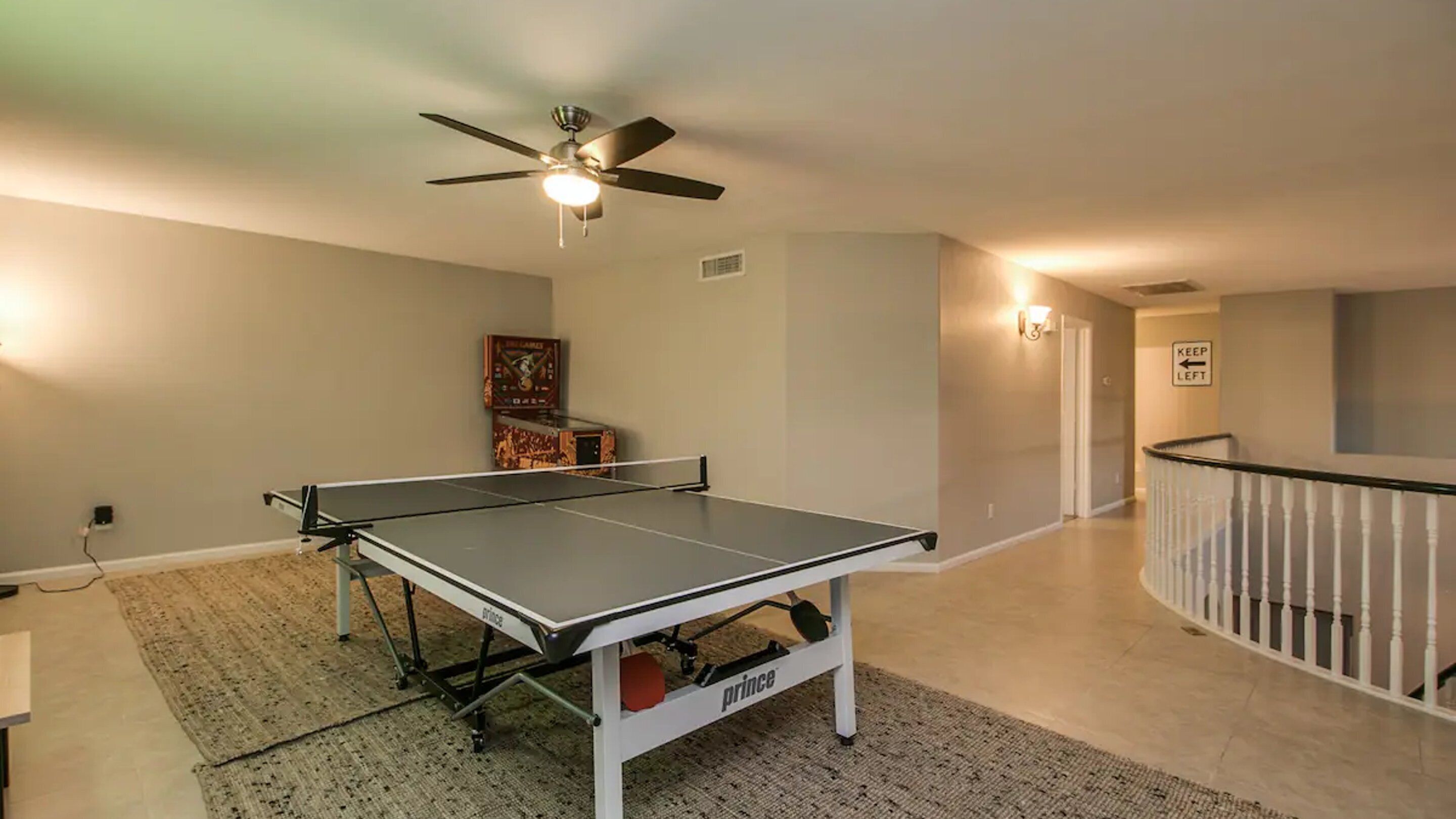 Taula de ping-pong en una habitació amb ventilador de sostre, una catifes i unes escales.