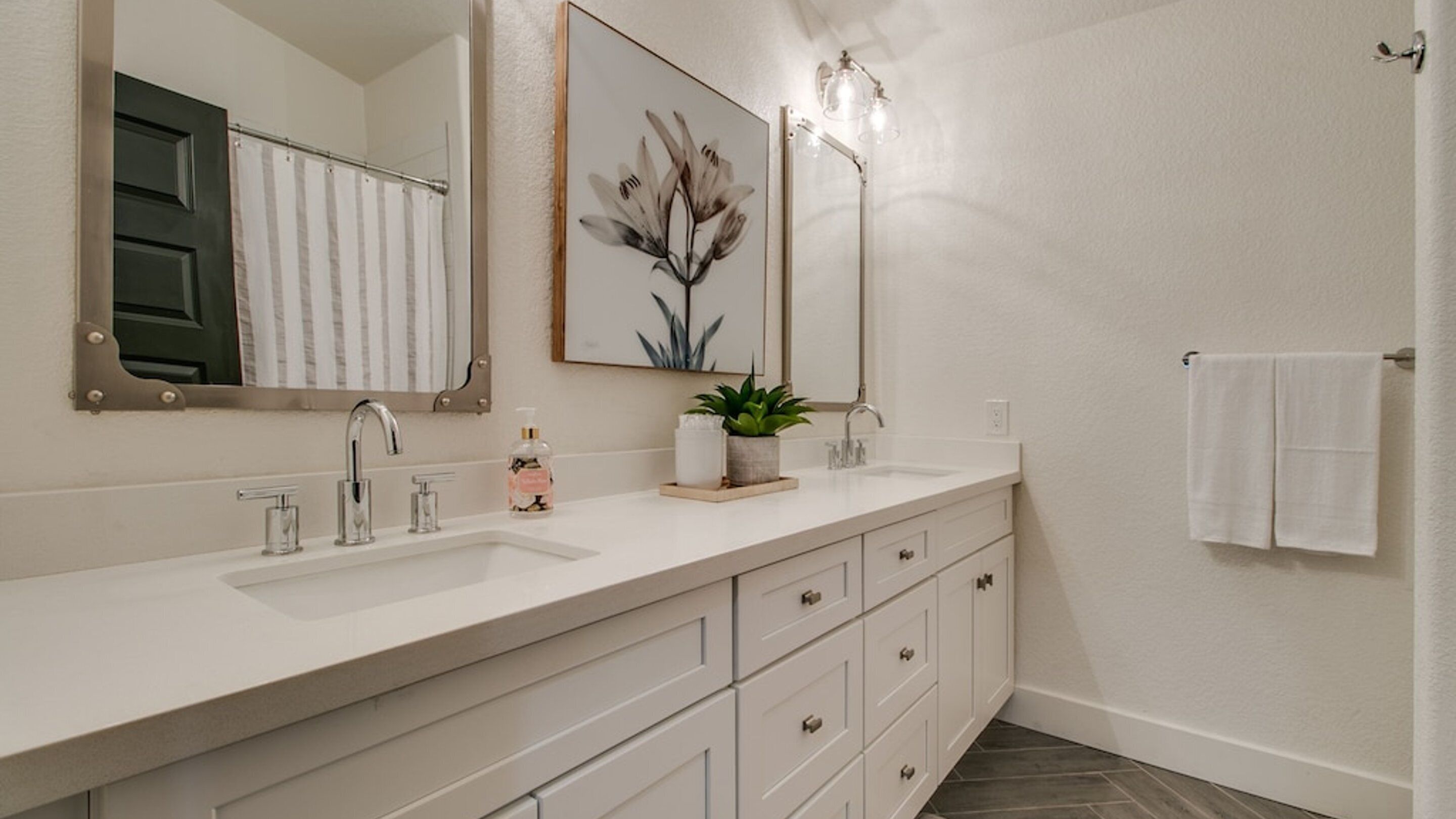 A bathroom with a double sink, a mirror, a towel rack, and a potted plant.