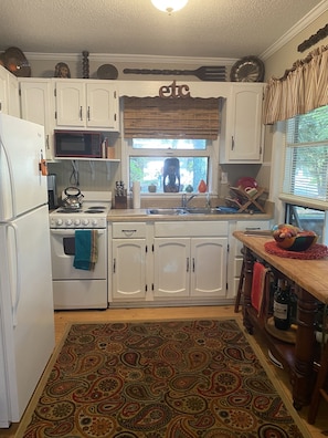 A kitchen with white cabinets, a microwave, a stove, and a window with a view of greenery.